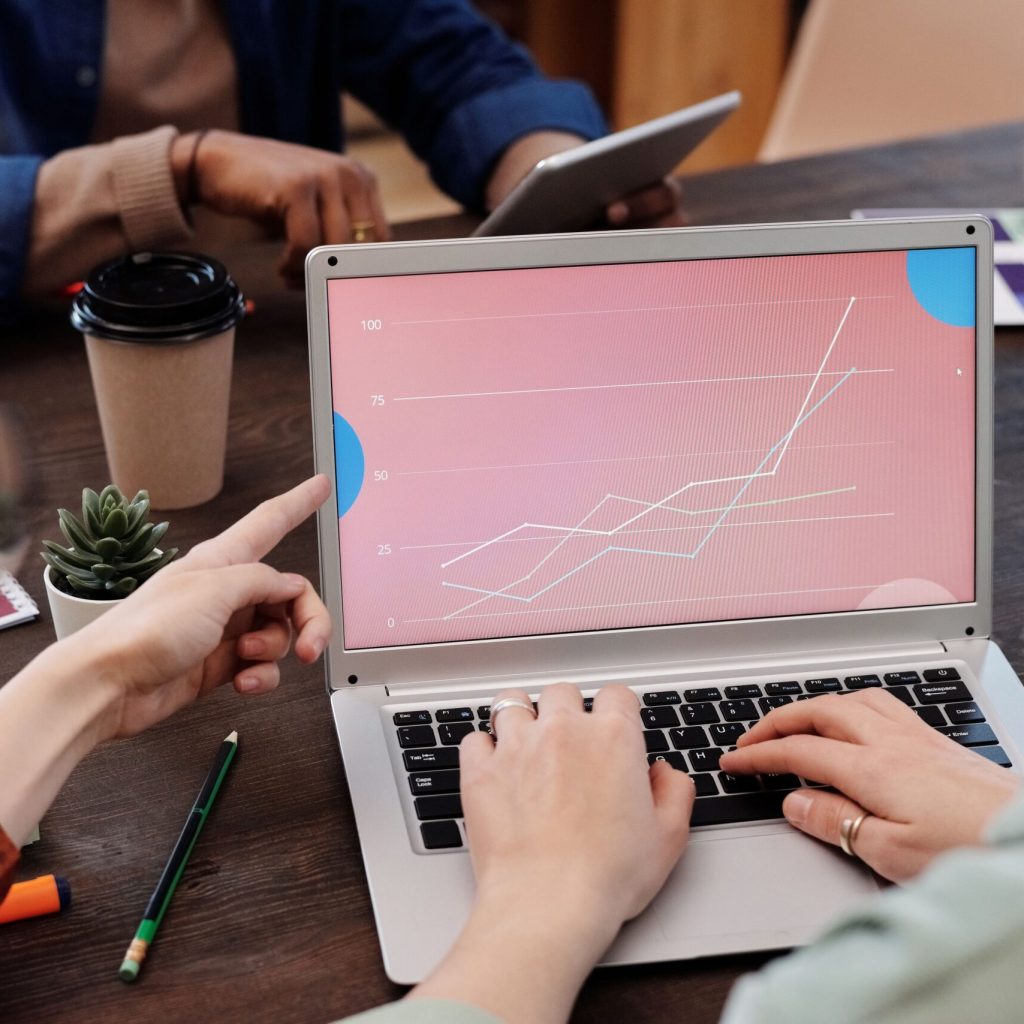 Office workers collaboratively reviewing data trends on a laptop during a meeting.